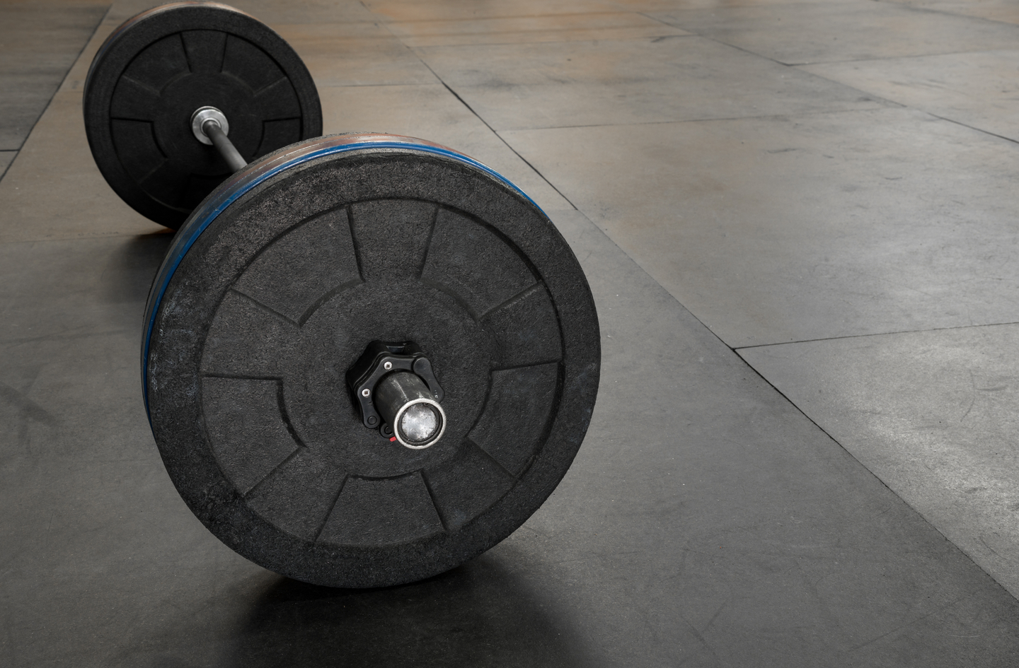 Basement gym flooring: barbell with bumper plates resting on textured rubber gym flooring