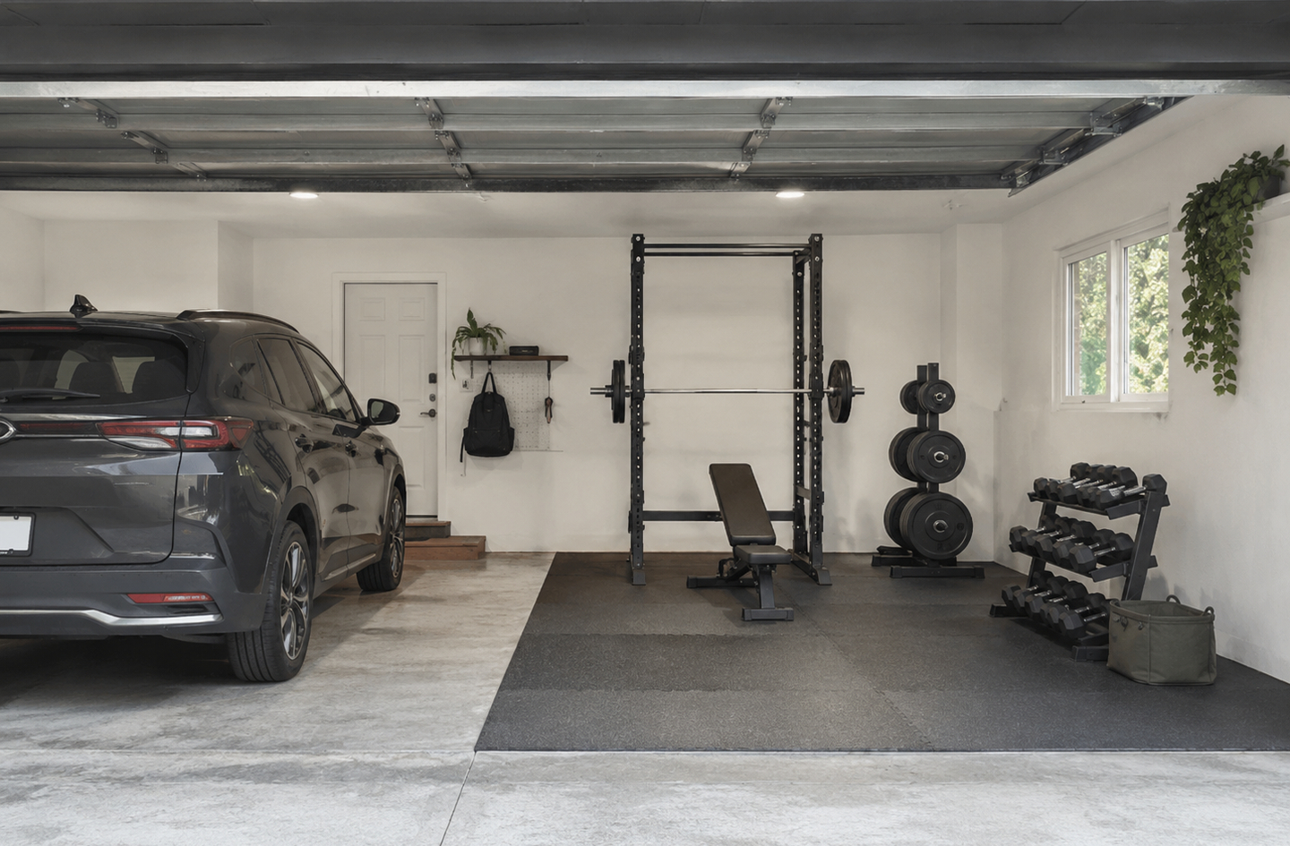 Squat rack and dumbbell rack set up in a shared garage space alongside a parked SUV, showing rubber floor mats on concrete and door clearance constraints