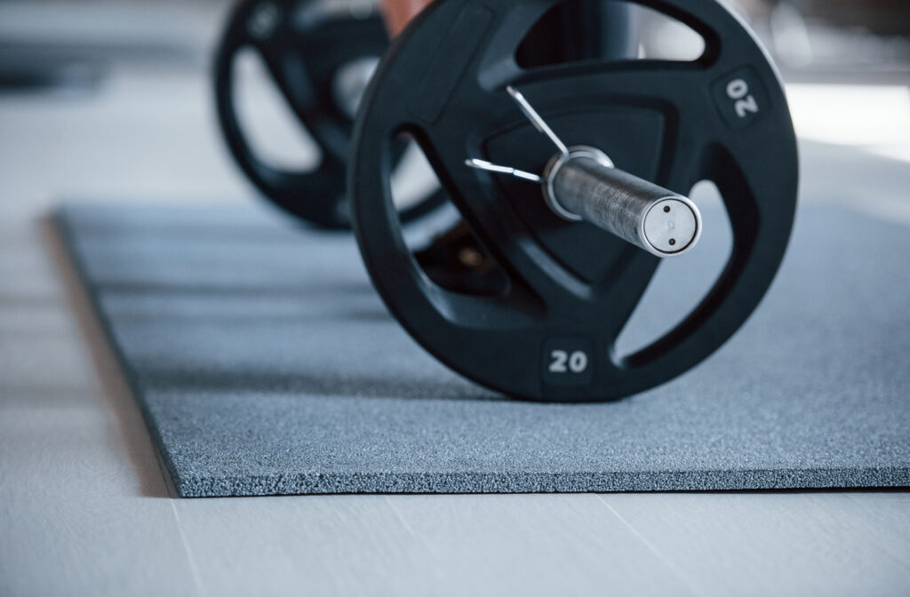 small home barbell with 20 kg weight plates resting on a rubber mat in a home training space