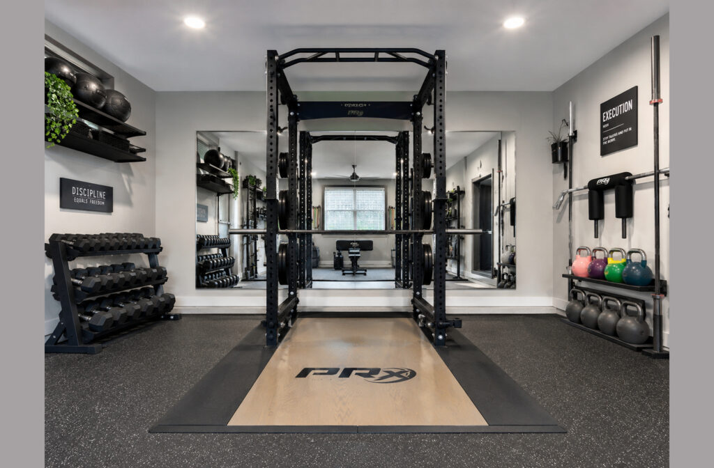 Strength zone design example with a power rack centered on a wooden lifting platform, rubber floor, barbell wall mounts, and dumbbell storage